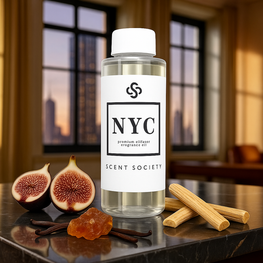 Clear 100ml bottle of Scent Society's NYC diffuser oil standing on a reflective marble surface in front o a blurred high-rise city window backdrop. A halved fig sits beside the bottle, with rich purple lesh exposed, suggesting a deep, sophisticated scent profile. The bottle features a white label with bold black 'NYC' text and the Scent Society logo.