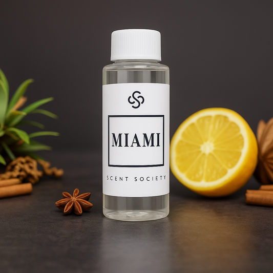 Clear 100ml plastic bottle of Scent Society MIAMI premium diffuser oil, labeled in white with black text placed on a dark stone surface surrounded by a fresh lemon half, cinnamon sticks, star anise, and green leaves, suggesting a warm citrus and spice fragrance inspired the by One 1 Hotel.