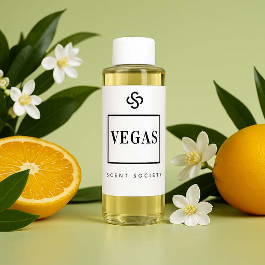 Clear 100ml bottle of Scent Society's Vegas Diffuser oil displayed against a soft green background, surrounded by white orange blossom flowers and fresh oranges, including one sliced open The bottle features a clean white label with the Scent Society logo and bold text reading 'Vegas' evoking a bright, citrusy scent experience.