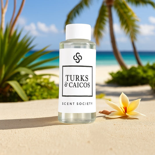 Scent Society TURKS & CAICOS premium diffuser fragrance oil in a clear 100ml plastic bottle with white label and cap, placed on a sandy surface with a yellow tropical flower in the foreground and palm trees, greenery, and a turquoise ocean in the background.