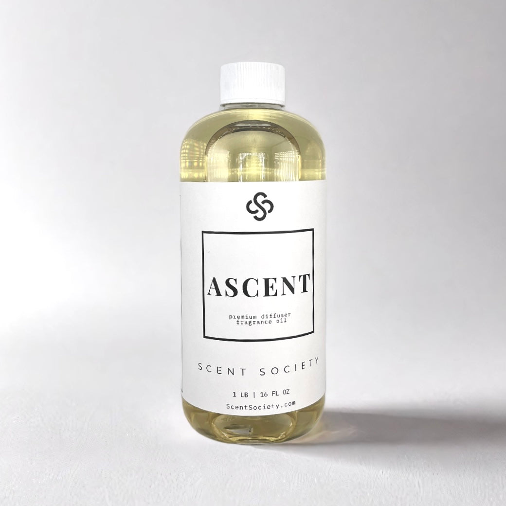 500ml bottle of Scent Society Ascent diffuser oil on a neutral background. Clear plastic bottle with white cap and minimalist black-and-white label, filled with fragrance oil. Aromatherapy oil for use in cold air diffusers.