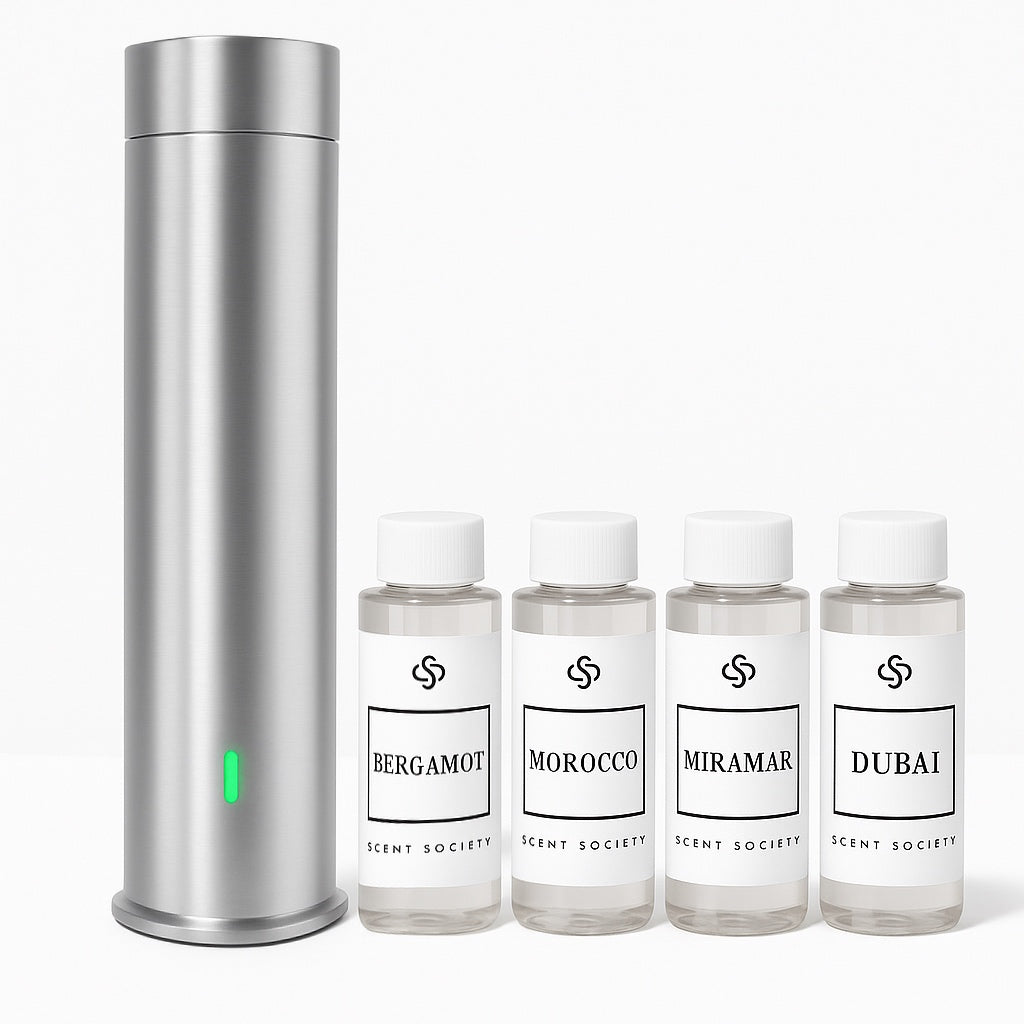 Silver Scent Society Tower Diffuser with Green LED light standing next to four fragrance oils in clear bottle, white labels and white caps. The fragrance names are Bergamot, Morocco, Miramar, Dubai
