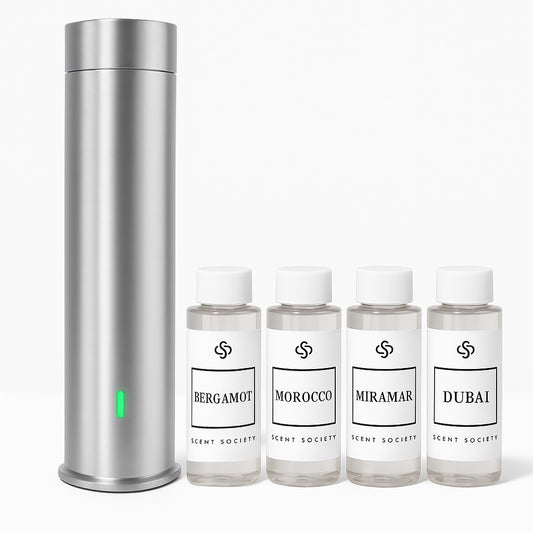Silver Scent Society Tower Diffuser with Green LED light standing next to four fragrance oils in clear bottle, white labels and white caps. The fragrance names are Bergamot, Morocco, Miramar, Dubai