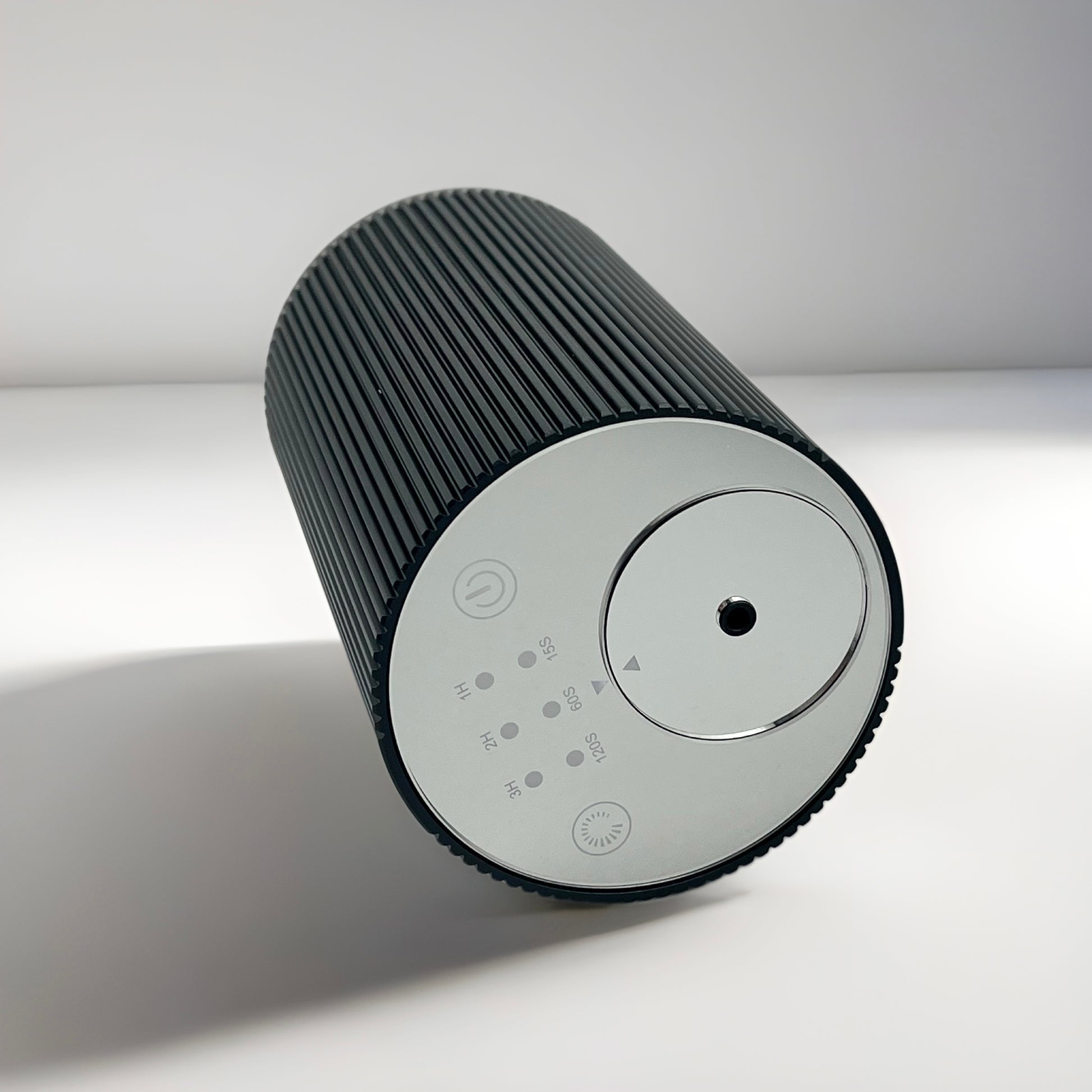 Black Scent Society Entrance Scent Diffuser cylindrical device laid on side with mirror control panel on a white background.