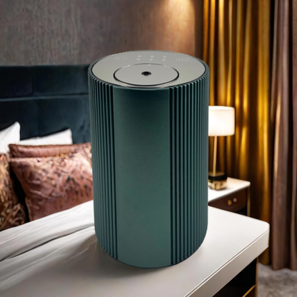 Scent Society Intro compact green diffuser with vertical ribbed texture, flat circular top, and LED indicator lights, shown standing upright on a white nightstand in a luxury bedroom with velvet pillow gold curtains and ambient lighting.