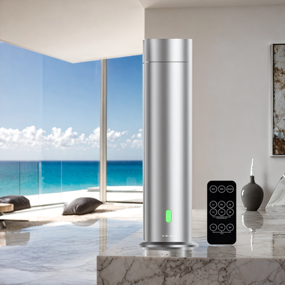 Silver scent diffuser with black remote control, placed on a marble surface overlooking a luxury beachfront view — high-end home fragrance machine for large spaces.