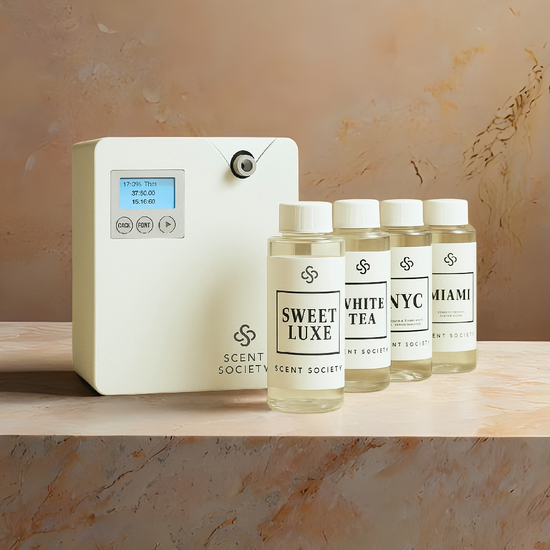 Scent Society diffuser and bottles on a wooden surface with a neutral marble background. Founder Diffuser machine and Sweet Luxe, White Tea, NYC, Miami fragrance diffuser oils.