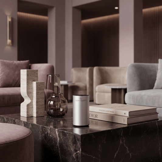 Modern interior with taupe colors and sofas in the foreground, a coffee table displaying decorative items and books and a centered silver Scent Society diffuser.