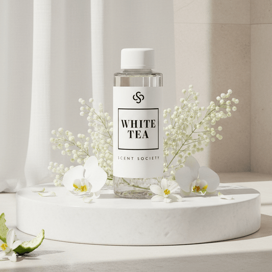 Bottle of 'White Tea'
diffuser oil fragrance from The Scent Society on a white surface with flowers and a lime.
